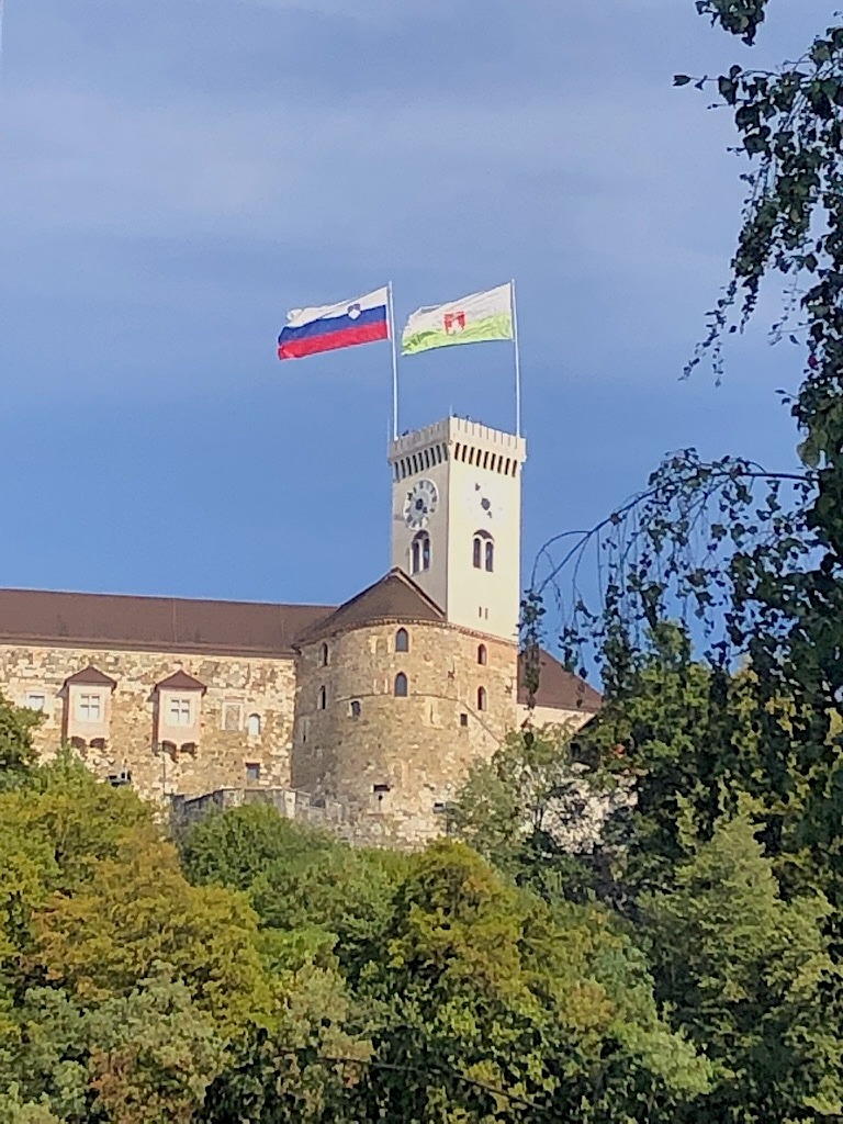 Castello di Lubiana visto dal basso tra gli alberi, con le bandiere slovene sulla torre