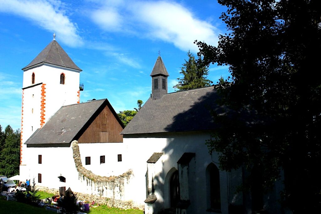 Piccola chiesa bianca con campanile a punta tra gli alberi nel bosco del Pohorje, Slovenia