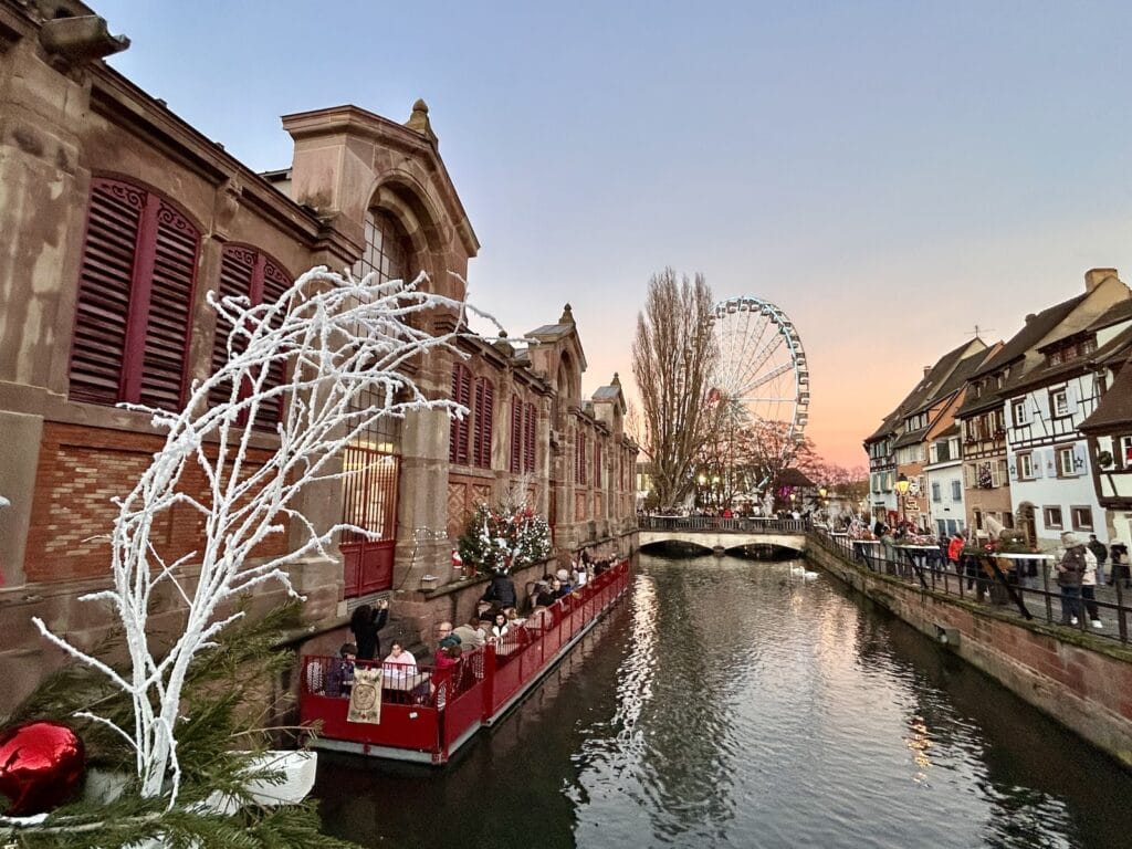 Ruota panoramica e canali di Colmar addobbati per Natale al tramonto, atmosfera magica in Alsazia.