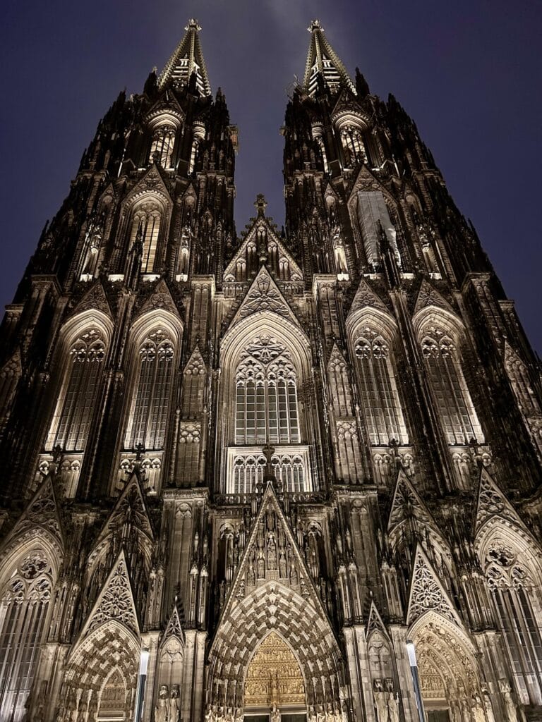Facciata illuminata del Duomo di Colonia sotto una fitta nevicata serale in inverno.
