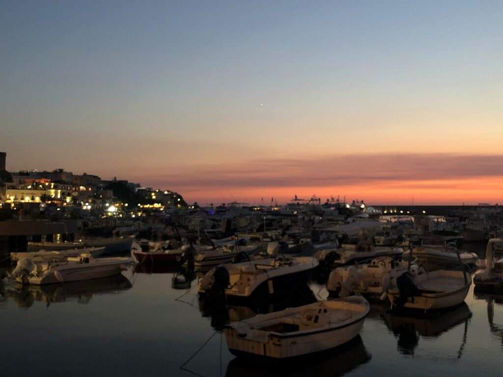Porto di Forio a Ischia al tramonto, barche ormeggiate e paese illuminato sullo sfondo
